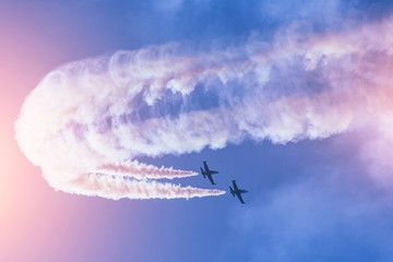 Couple of fighter jets flying against a bright sky, performing figures turns from the smoke.