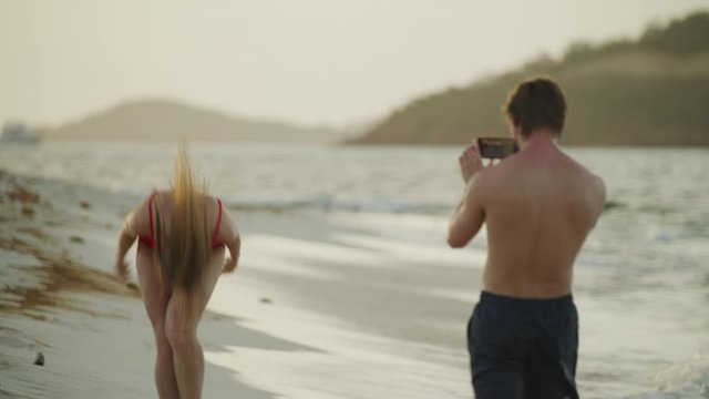 Man with cell phone photographing woman on ocean beach / Petit Tabac, Tobago Cays, St. Vincent and the Grenadines