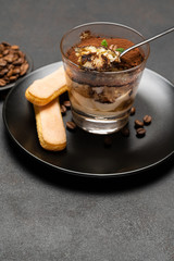 Portion of Classic tiramisu dessert in a glass cup on dark concrete background