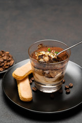 Portion of Classic tiramisu dessert in a glass cup on dark concrete background