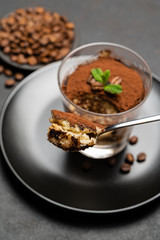 Portion of Classic tiramisu dessert in a glass cup on dark concrete background