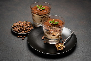 Portion of Classic tiramisu dessert in a glass cup on dark concrete background