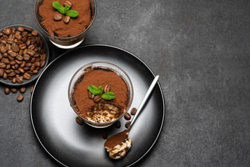 Portion of Classic tiramisu dessert in a glass cup on dark concrete background