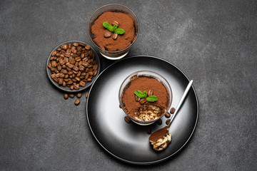 Portion of Classic tiramisu dessert in a glass cup on dark concrete background