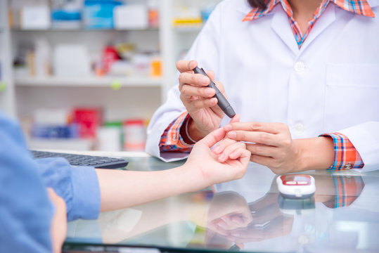 Hands of Pharmacist checking patient blood sugar by glucometer in drugstore