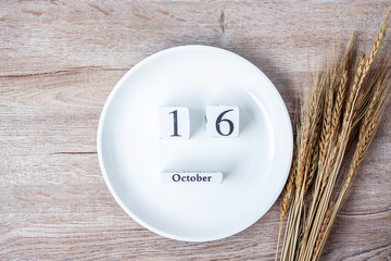 16 October calendar wooden with empty white plate and wheat on table background. Food Donation,...