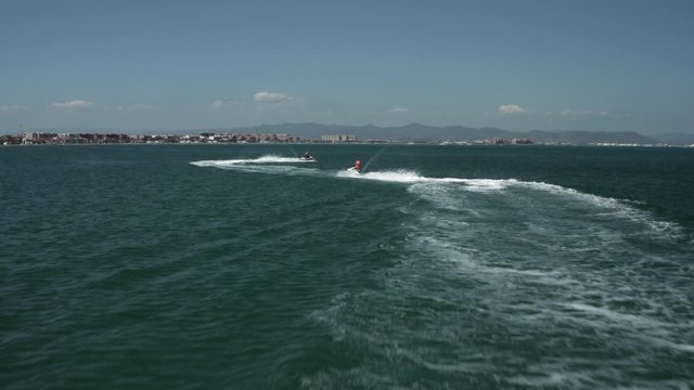 Aerial shot of two jet skis speeding on the water and making wide turns near coast