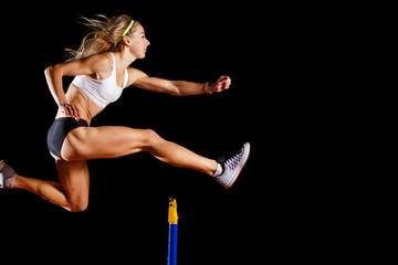 Sportswoman jumping over hurdle on sprint race