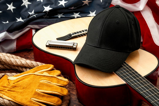 American culture, blues music and country music concept theme with a black baseball cap, USA flag, acoustic guitar, harmonica and a rope lasso on a wooden background in a old saloon