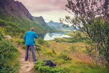 Fototapeta premium Młody człowiek robi zdjęcie zachodu słońca nad górskim jeziorem. Piękny skandynawski krajobraz górski. Widok na dolinę z jeziorem. Norwegia