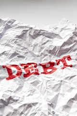 Wrinkled white paper with the word debt printed in red. Concept of debt free life or financial freedom. Vertical shot.