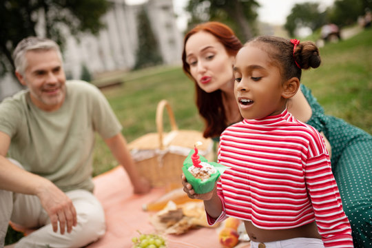 Dark-skinned daughter looking at little birthday muffin