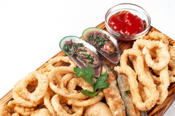 mussels and fried onion rings, squid and fried fish in batter on a cutting board with sauce, isolated on a white background