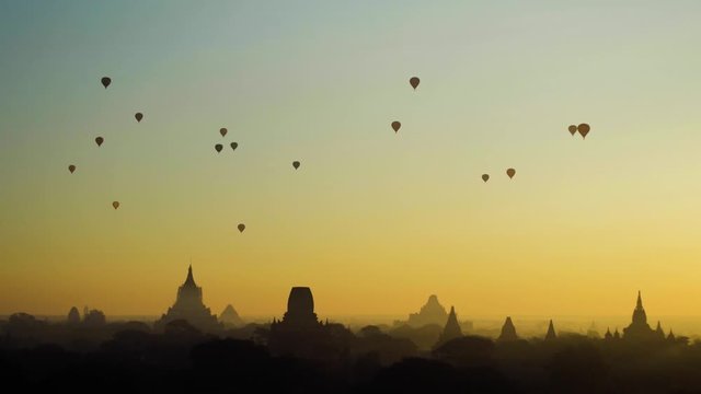 Landscape of silhouetted hot air balloons at early golden sunrise with temples in the background in Bagan, Myanmar
