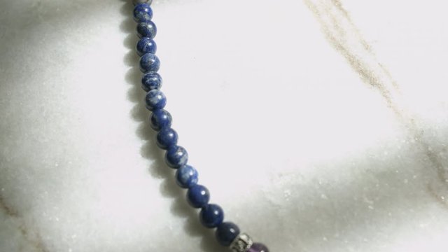 Macro dolly shot of blue lapis lazuli beads from a Tibetan prayer mala resting on white marble slab shot in UHD
