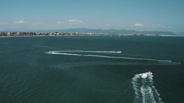 Aerial view of multiple jet skis speeding and making wide turns near coast, zoom out