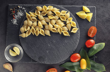 Pasta shells on black stone. Tomatoes and bay leaves with allspice and sea salt.