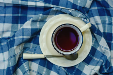 Top view: a cup of coffee, tea on a saucer and a teaspoon on a checkered napkin in blue and white. copyspace