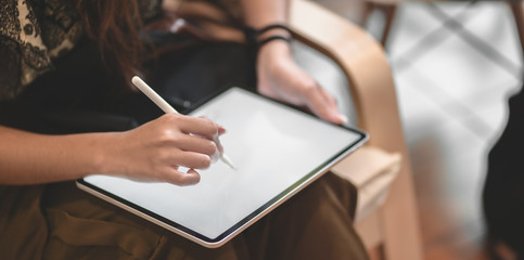 Close-up view of professional female designer working on her project while writing on tablet