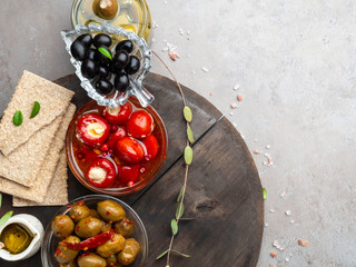 Italian food ingredients background with crackers, olive oil, mini bell peppers stuffed with cheese, olives and herbs on gray stone slate
