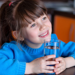 Adorable smiling little girl in blue sweater drinking water in kitchen. Health and beauty concept