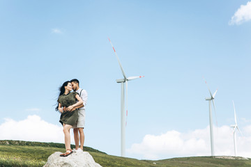 A young couple stands on the background of windmills and hugs. Close relationships and love between people.