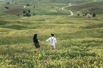 A young couple in a meadow spends time together. Summer holidays or carefree time. They run and have fun.