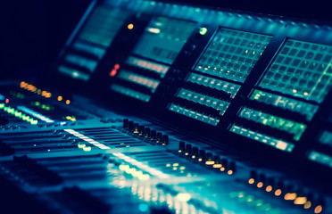 Professional concert sound mixer panel with sliders and regulators in blue stage lights