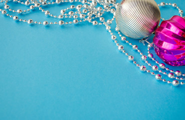 Decorative frame with silver beads, purple baubles and copy space for text. Merry Christmas and Happy New Year. Decorative garland on the blue background close up. Winter holidays and celebration.