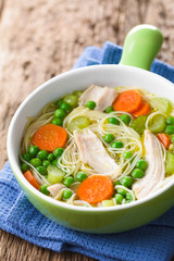 Fresh homemade chicken noodle soup with carrot, peas and celery in green soup bowl (Selective Focus, Focus in the middle of the soup)