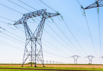 Dozens of electricity pylons in the countryside under a clear blue sky.