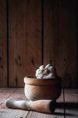 WHITE GARLIC WITH WOODEN MORTAR ON WOODEN TABLE AND DARK BACKGROUND. RUSTIC FOOD PHOTOGRAPHY.