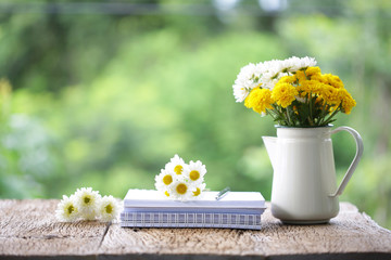 Flower in metal pot with diary on wooden table at outdoor 