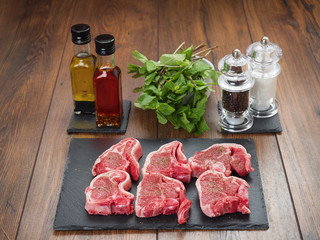 Six raw lamb chops on a slate plate, Infused oils , herbs, salt and pepper shaker on a wooden table surface.