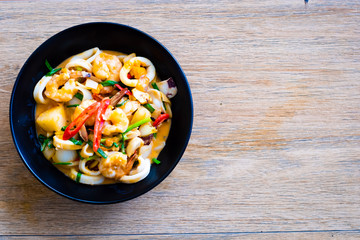 Stir Fried Squid with Salted Eggs on black plate on wooden table , Thai food.