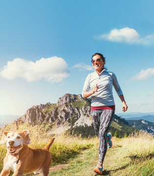 Happy smiling female jogging by the mounting range path with her beagle dog. Canicross running healthy lifestyle concept image.