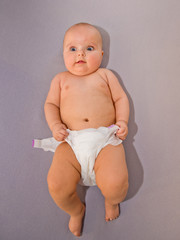 Baby takes off his diaper on grey background. Top view.