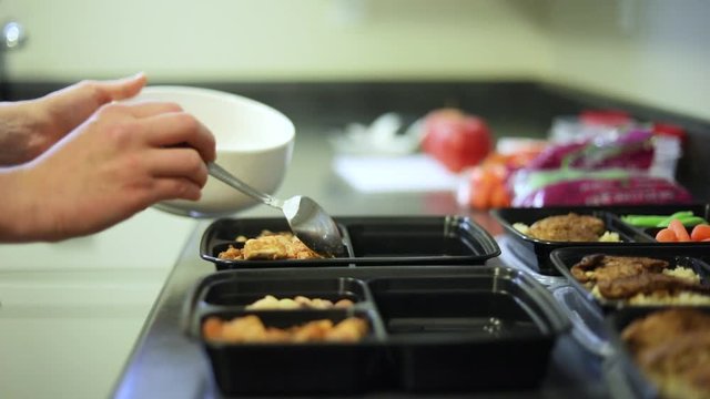 Slow Motion shot of someone doing weekly meal planning. The meals are divided by day and contain carrots, edamame, and grilled chicken on brown rice.