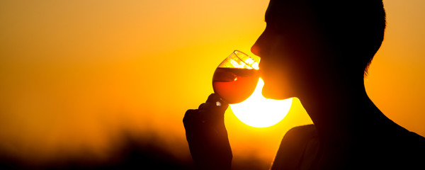 Woman with a cocktail over suset sky in orange colors.