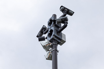 Black video monitoring cameras and street lamps on column against white sky