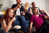 Group Of College Students In Shared House Watching TV And Eating Popcorn