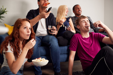 Group Of College Students In Shared House Watching TV And Eating Popcorn