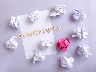 White paper with wastepaper -one of different colour - on a violet background. The word creativity in wood