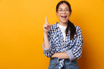 Happy emotional surprised cute teenage girl in glasses posing isolated over yellow wall background...