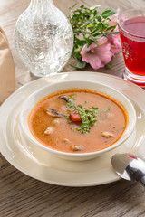 Hot and sour soup Tom Yum Goong with tomatoes and champignon and red drink on wooden table