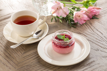 Strawberry jam in a jar and cup of black tea on wooden table