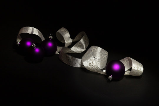 Purple Christmas balls and white ribbon on black background