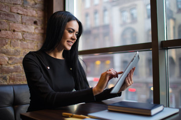 Confident woman intelligent government worker checking e-mail on portable touch pad computer while sitting at workplace in office interior. Female economist using digital tablet for online chat  