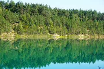 Fototapeta na wymiar Pine forest is reflected in the surface of the green-blue water of the chalk pits in the center of Belarus, Lyuban