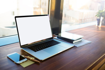 Workplace with open pc laptop computer with blank monitor background for advertising text message lying on a wooden table near mobile phone and working tools in modern coworking space.
